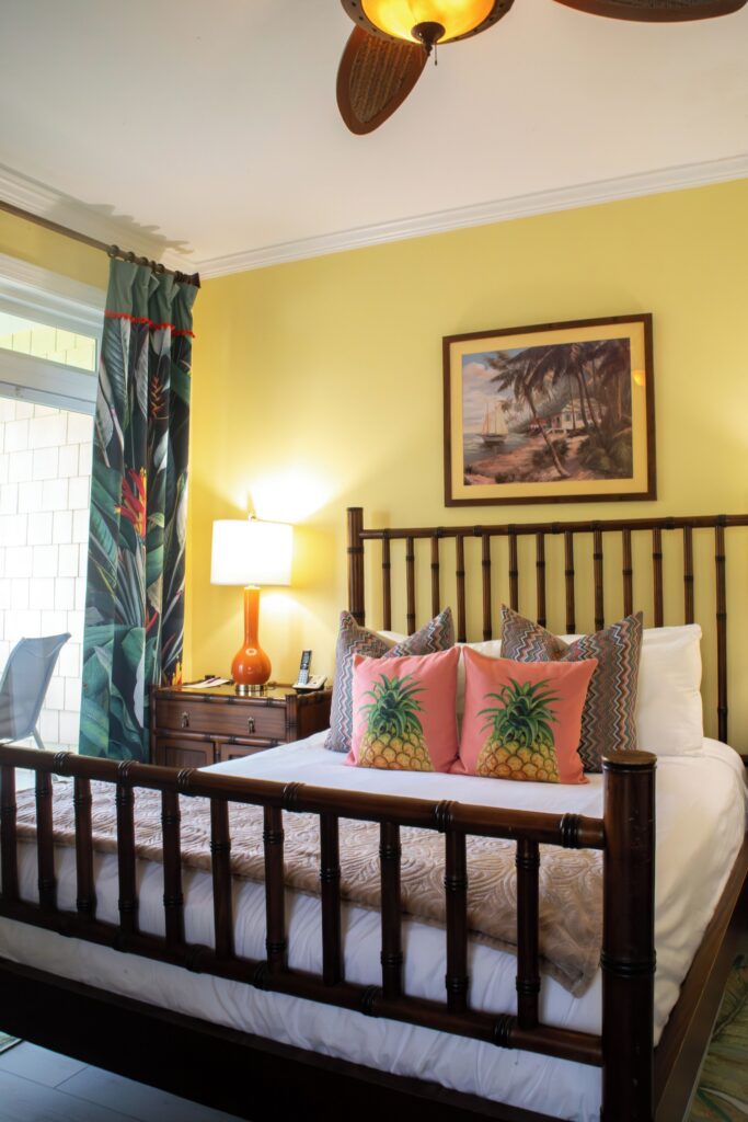 Guest room with a dark wood bed and tropical art at Water’s Edge Inn